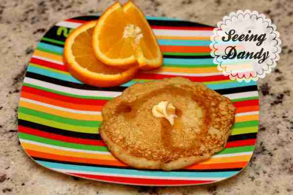 Delicious homemade pancakes recipe served withs sliced oranges on a colorful striped plate.