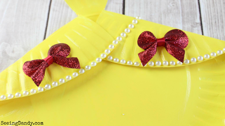 Adding red bows and pearl beads to DIY Belle dress.