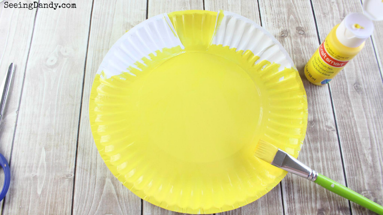 Painting DIY Belle dress paper plate craft with yellow paint.