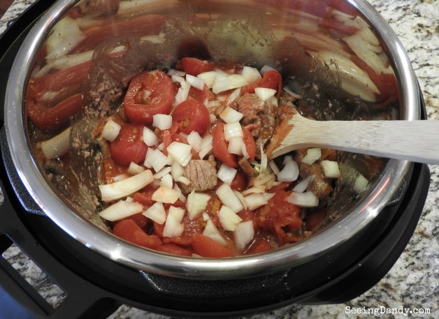 Stirring Instant Pot round steak with onions and tomatoes.