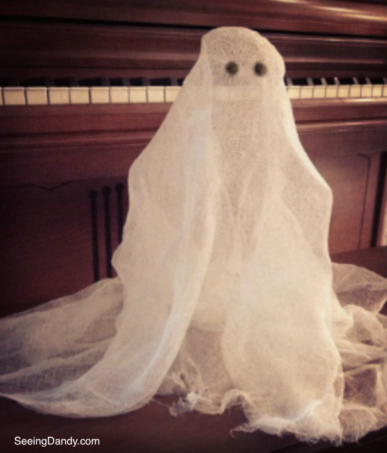Haunting cheesecloth ghost standing up on piano bench.