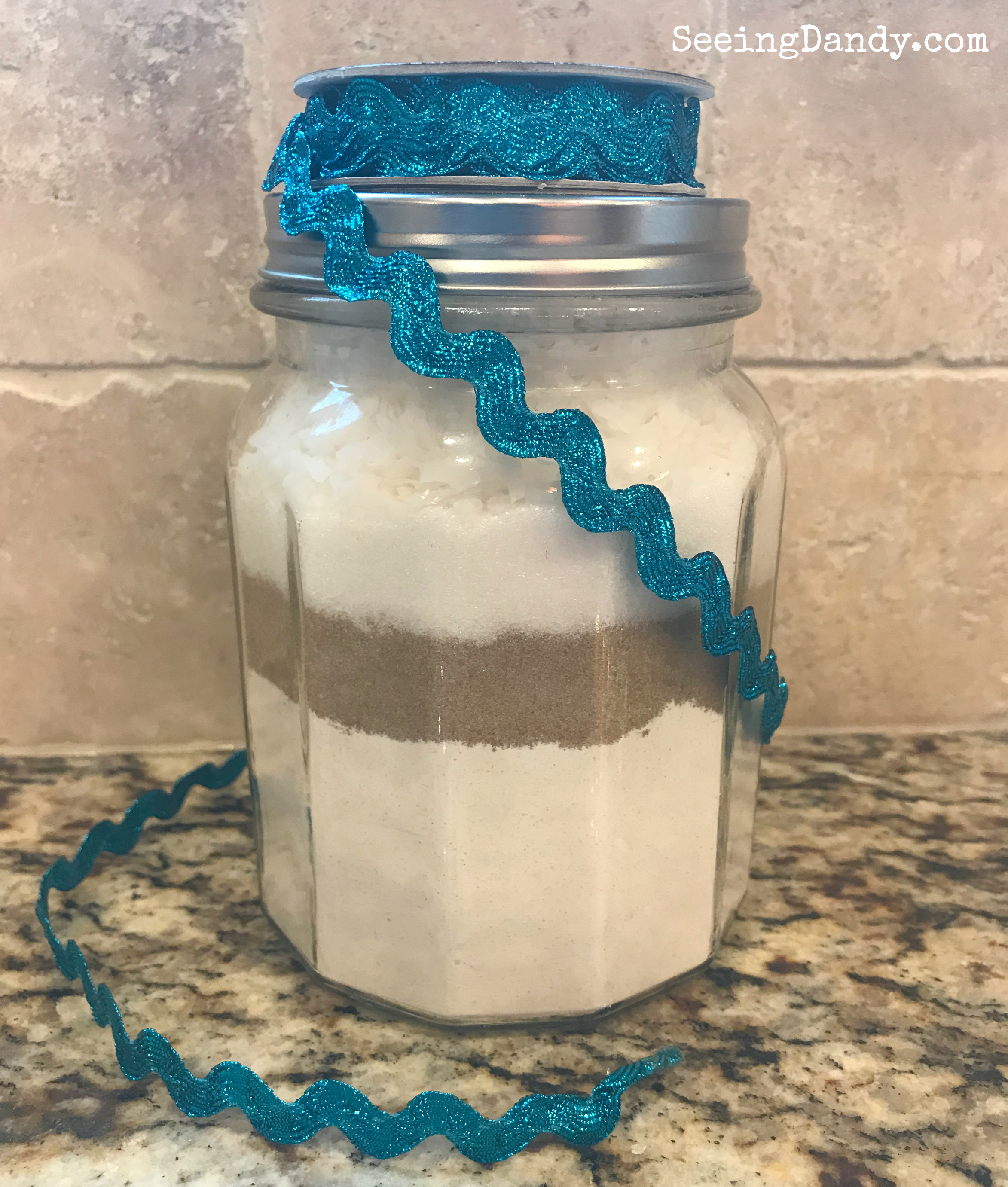 Snowflake cookies in a jar ingredients and layers with blue ribbon.