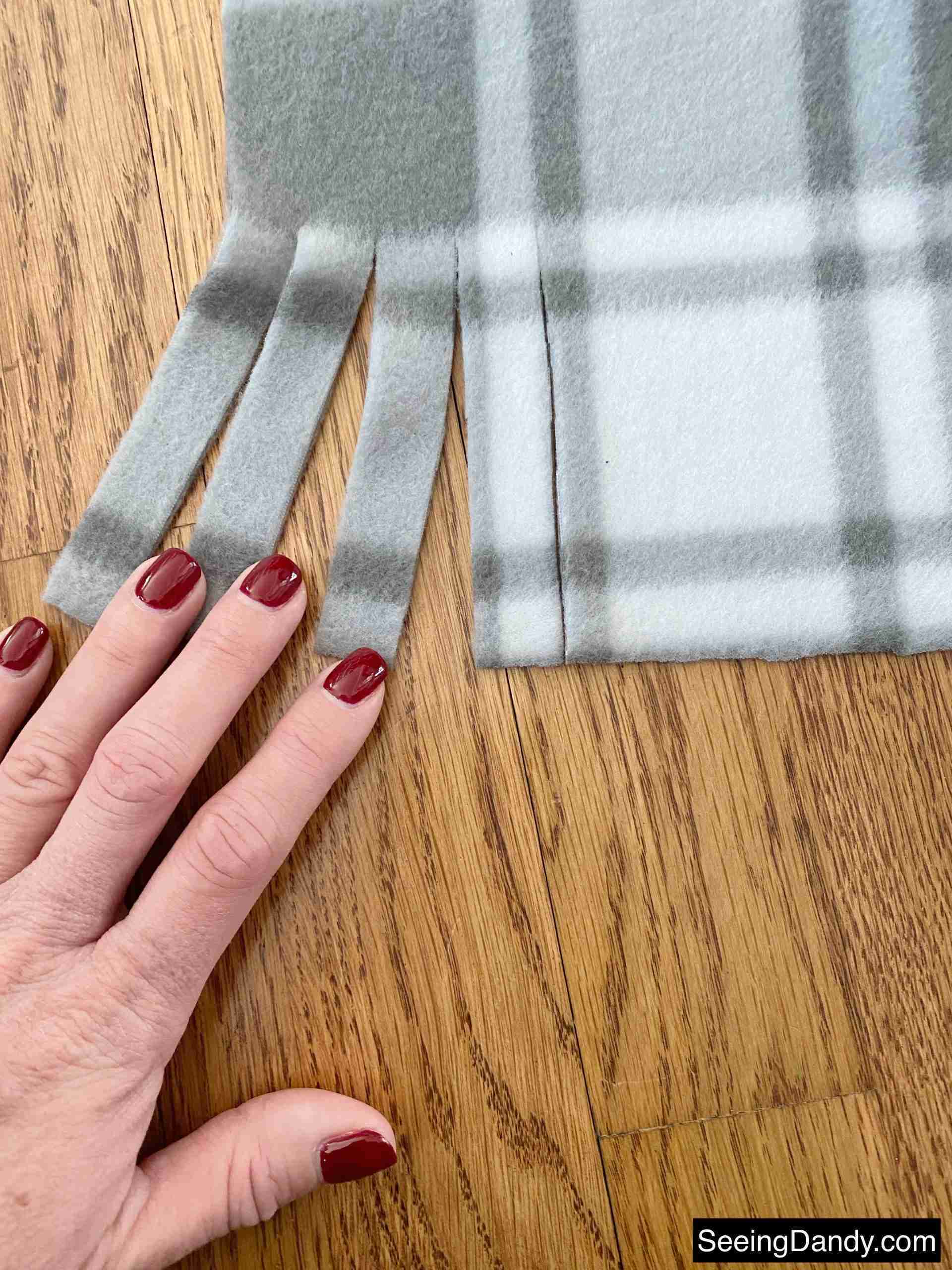 cutting scarf fringe, red purple gel nail polish, hardwood floor, plaid gray white fleece fabric