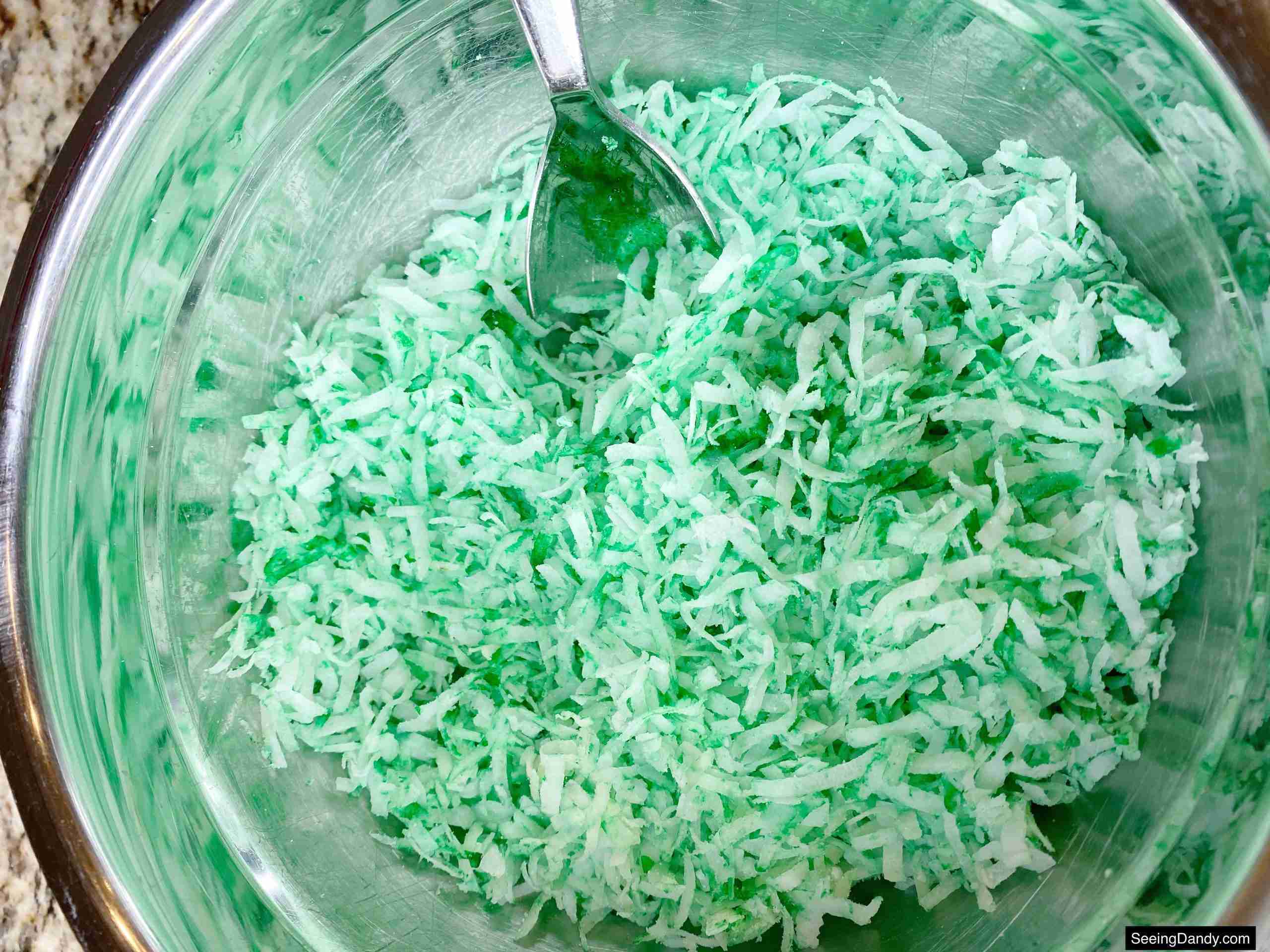 green food coloring, sweetened coconut flakes, silver mixing bowl, silver spoon