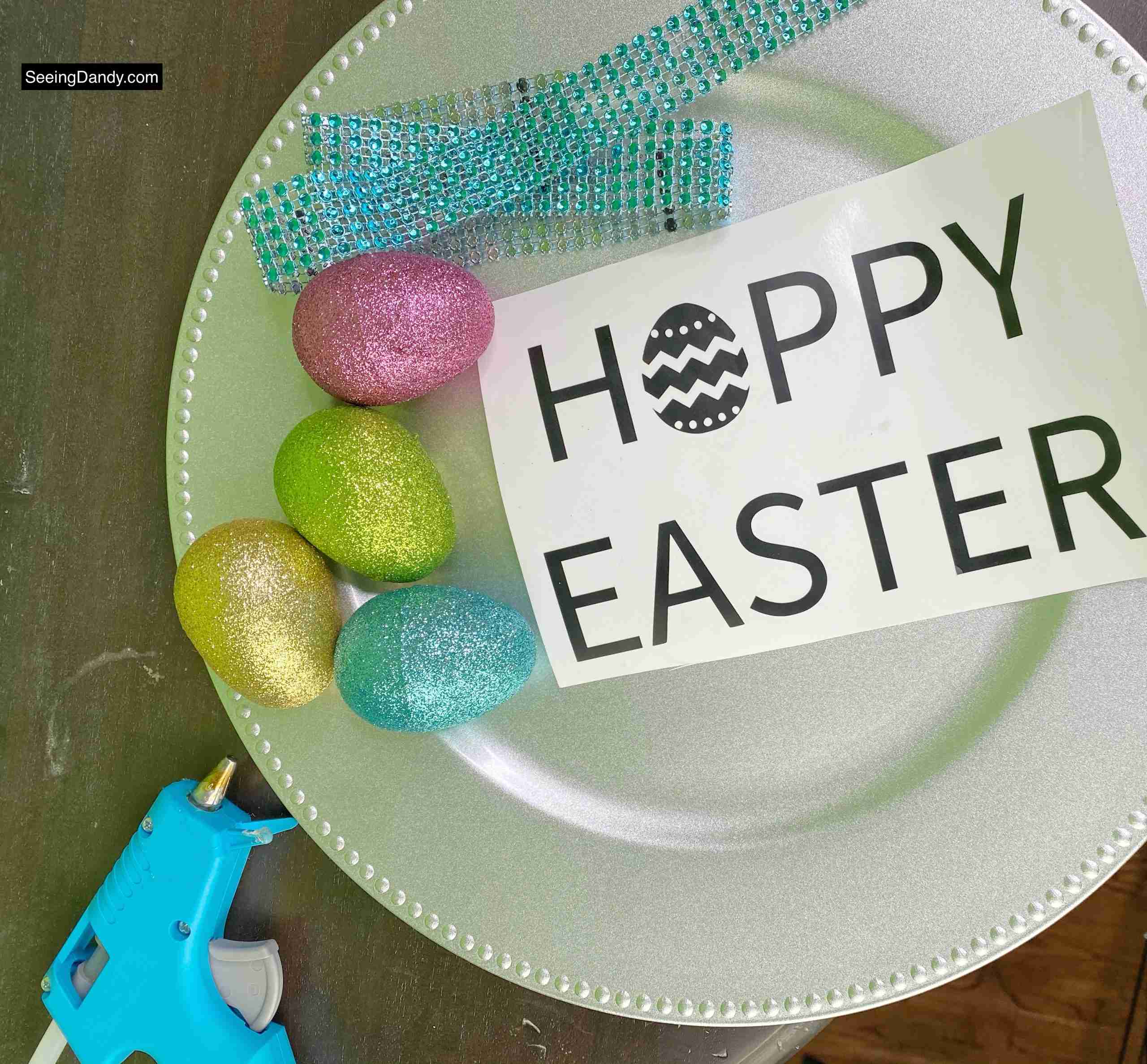 free svg file, dollar tree glitter easter eggs, happy easter svg file, hoppy easter svg file, vinyl craft idea, silver charger plate, dollar tree plastic charger plate, glue gun, teal jeweled ribbon