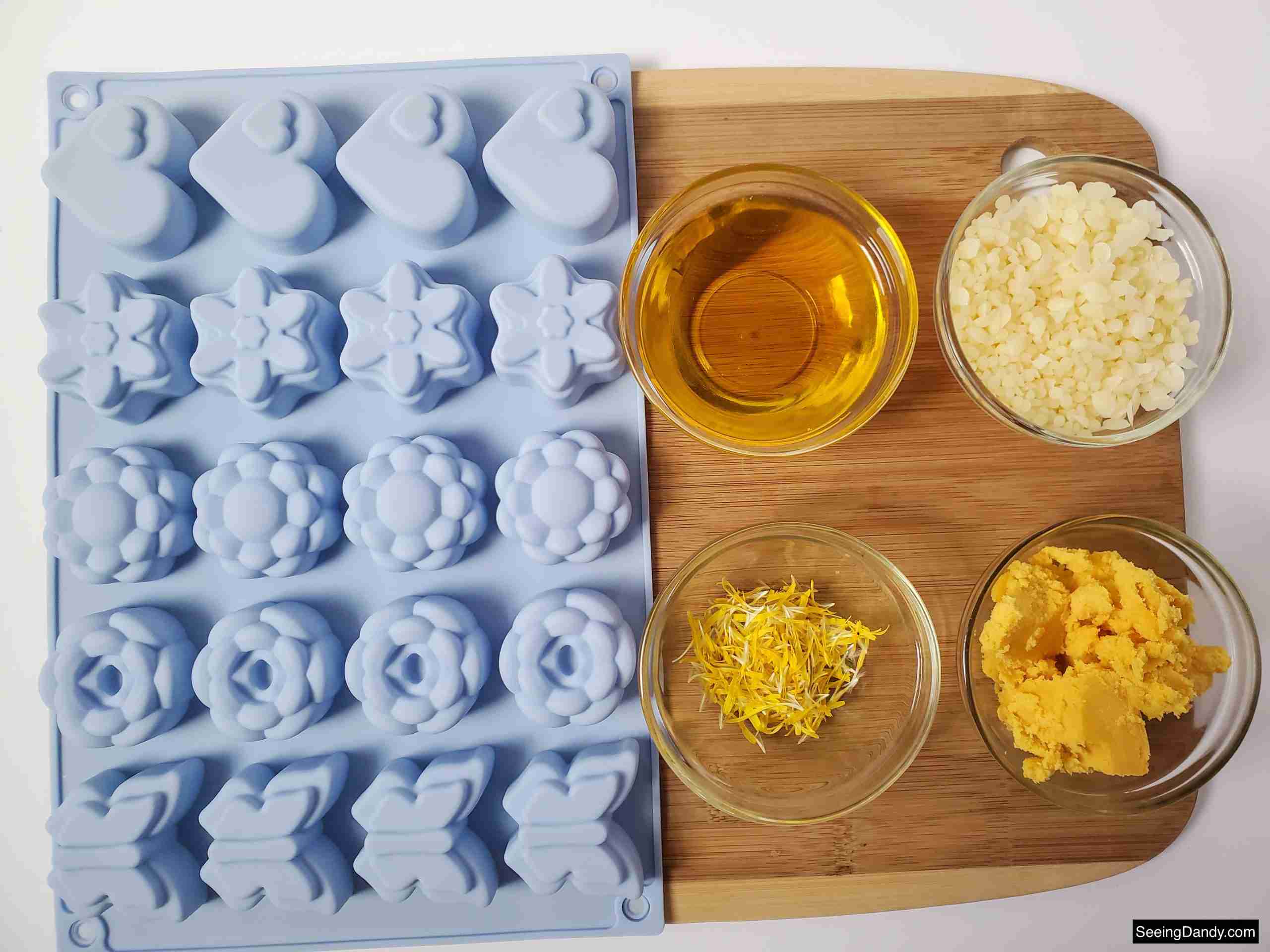 wood cutting board, glass mixing bowls, shea butter, beeswax, dandelion infused oil, fresh dandelion petals, silicone flower soap mold
