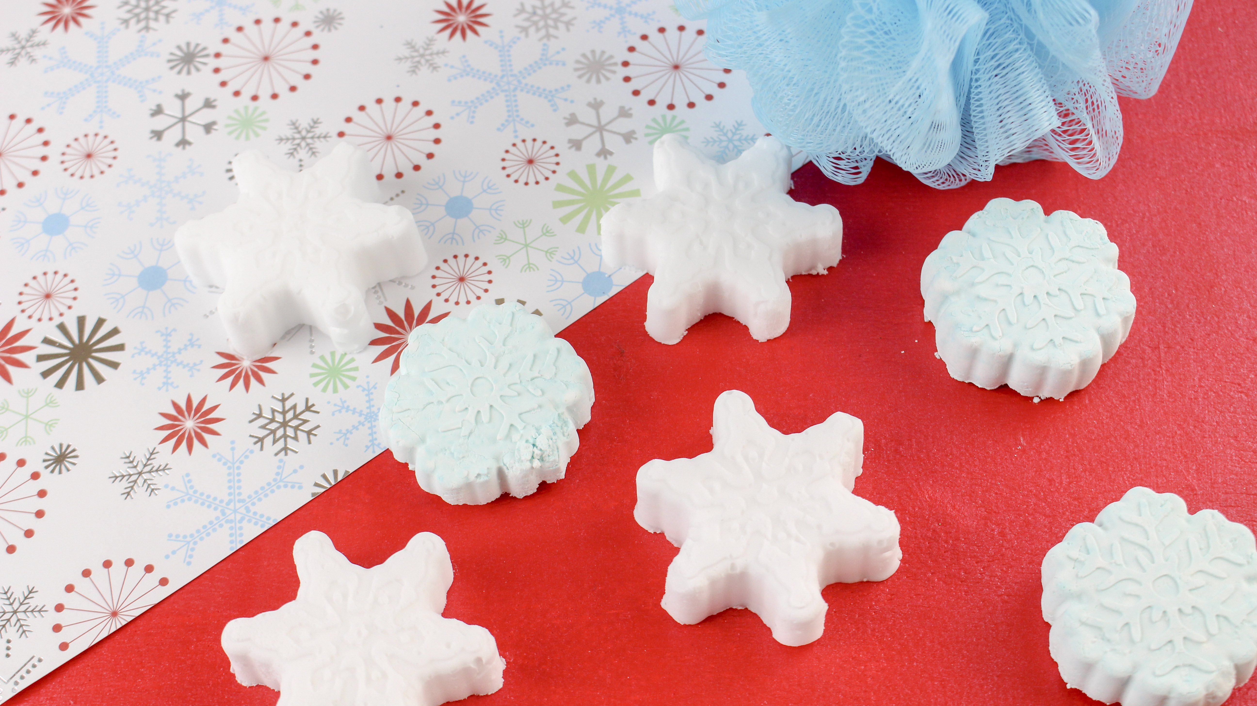 Snowflake peppermint shower steamers on festive paper with blue body wash pouf.